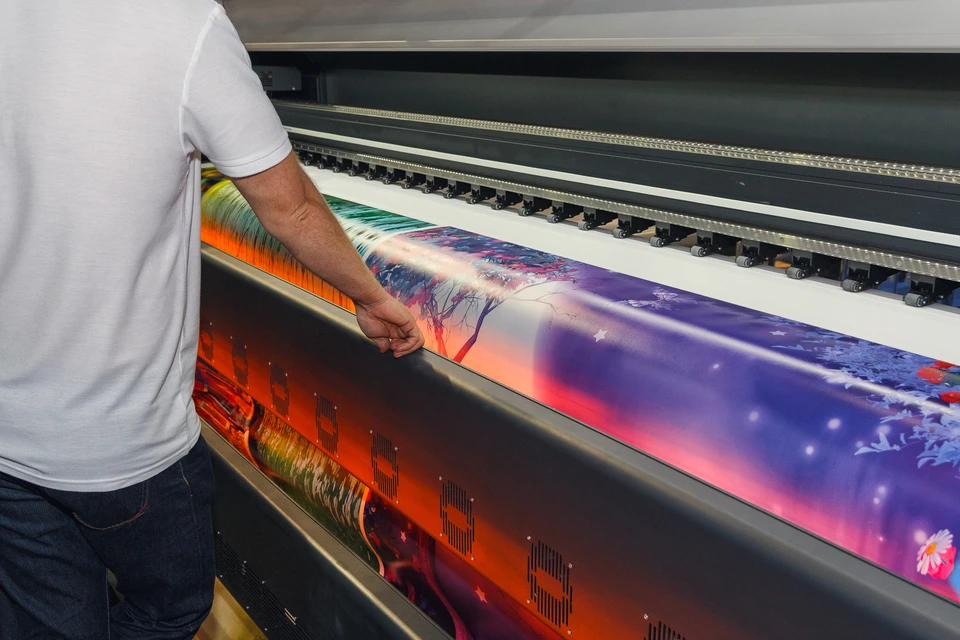 Un homme en t-shirt blanc supervise l'impression grand format sur une imprimante à jet d'encre industrielle