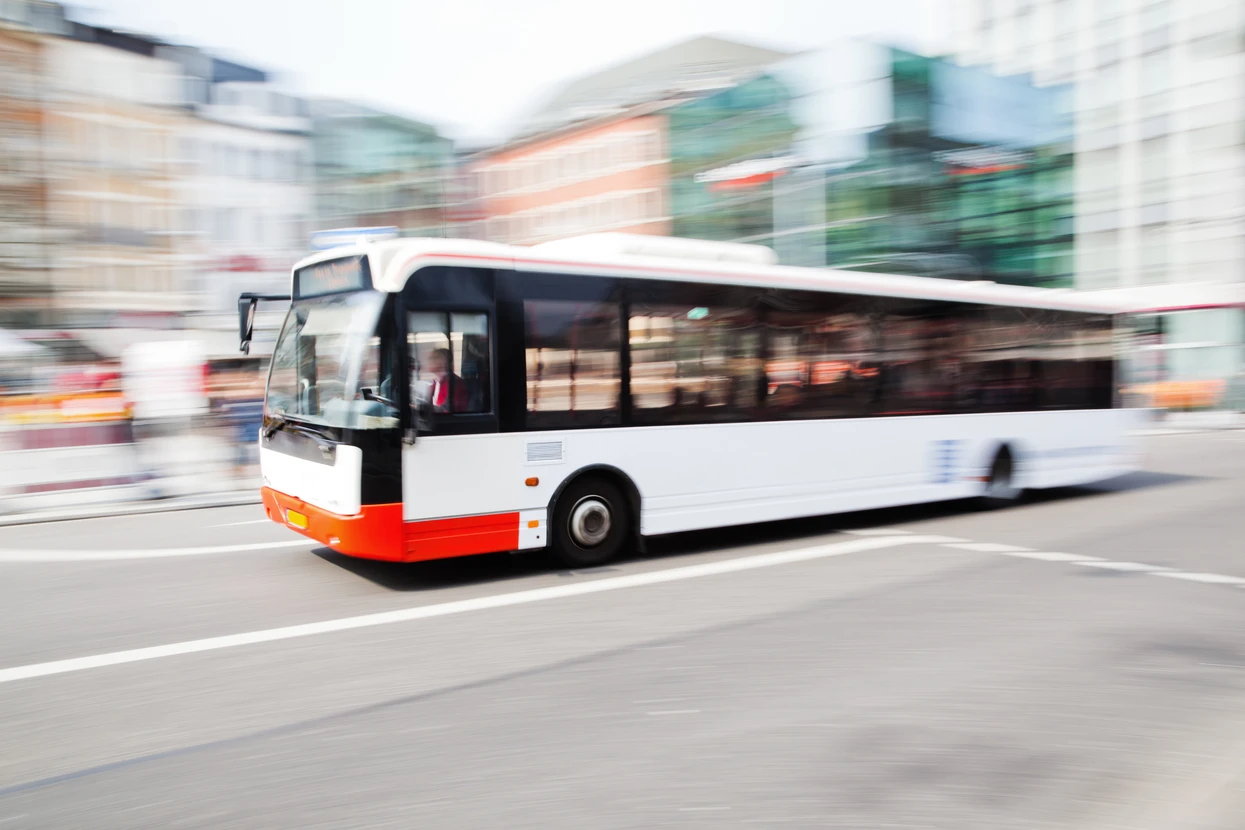 Autobus urbain blanc et orange en mouvement sur une route urbaine avec bâtiments en arrière-plan flous