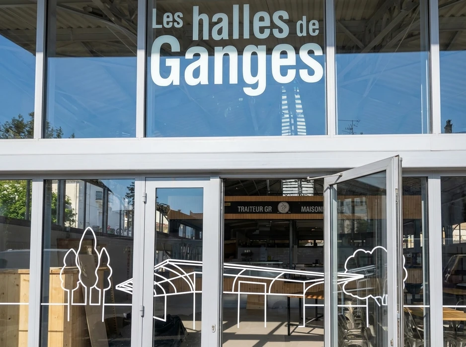 Façade vitrée d'un établissement commercial nommé "Ganges", avec portes coulissantes en aluminium blanc ouvertes