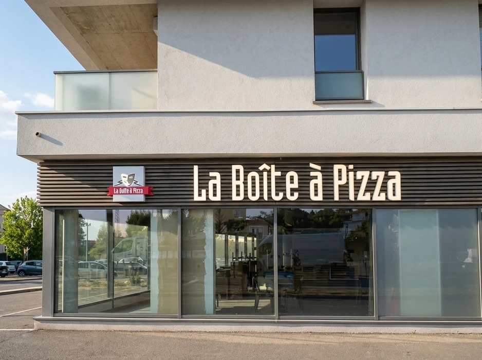 Façade extérieure d'une pizzeria franchisée **La Boîte à Pizza**, enseigne lumineuse en lettres volumétriques blanches rétroéclairées, logo théâtral rouge et blanc