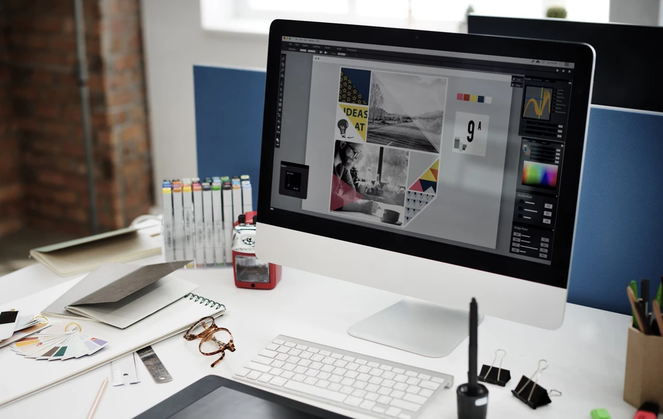 Bureau de designer graphique moderne avec iMac affichant un projet de création visuelle comprenant photographies, typographies et éléments colorés
