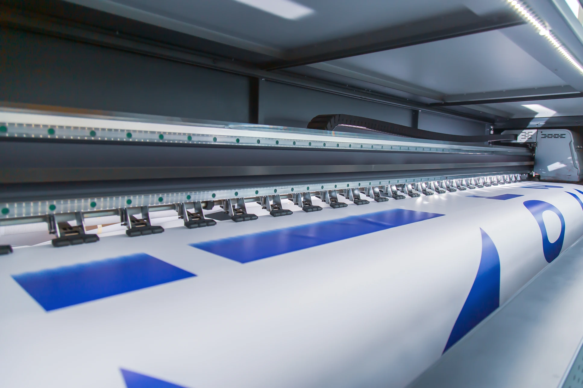 Photographie d'un espace d'atelier professionnel moderne montrant un artisan ou technicien travaillant devant une enseigne lumineuse LED partiellement installée ou en phase de réalisation, avec mise en avant des équipements de pointe (imprimante grand format, découpe laser visible en arrière-plan). La scène doit capturer l'expertise technique et la fabrication locale, avec une focus sur le savoir-faire en signalétique et enseignes lumineuses, éléments signatures de l'entreprise Atelier JPB Communication.