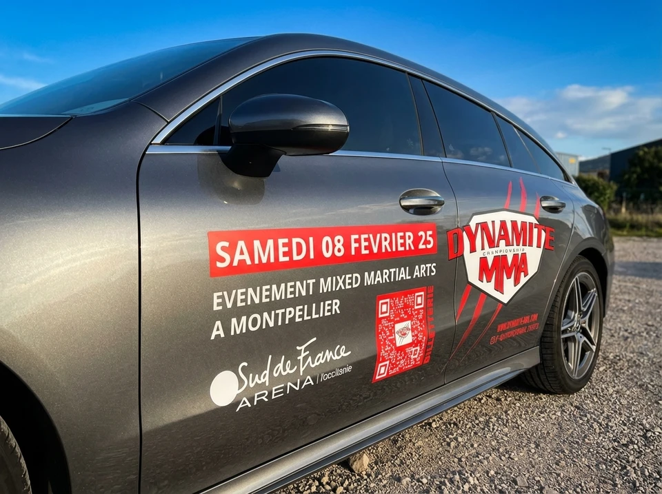 Technicien appliquant un film de protection transparent sur le pare-brise d'un véhicule noir dans un atelier automobile professionnel