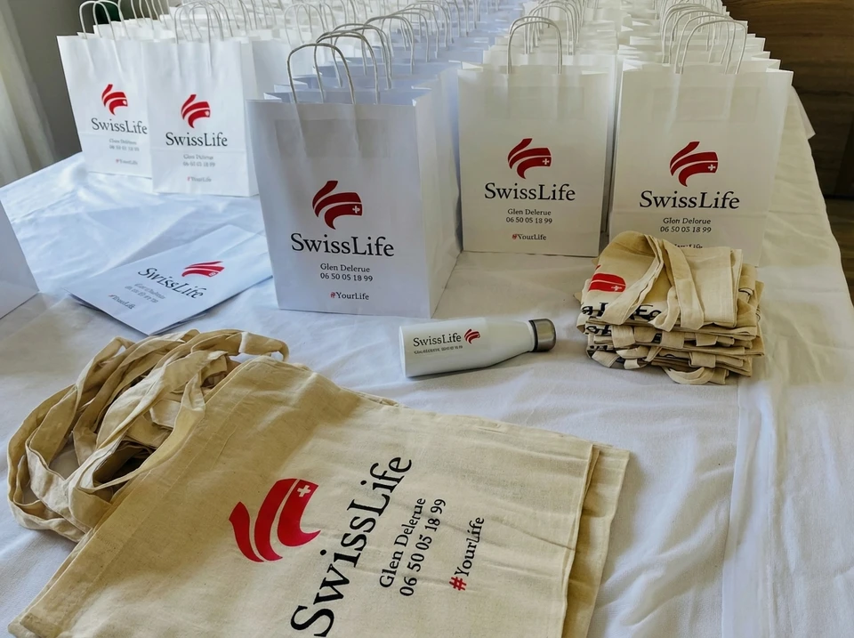 Présentation d'objets promotionnels sur surface en bois : t-shirt blanc, casquette bicolore blanc-orange, parapluie, mug, sac, clé USB, stylo et drapeau