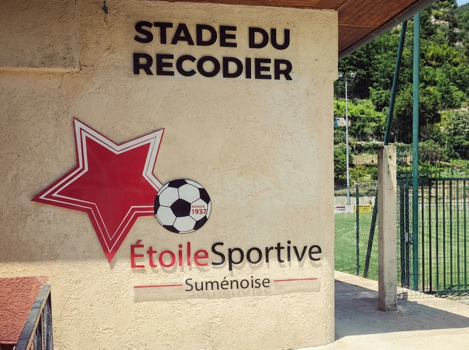 Enseigne commerciale blanche en relief avec lettres tridimensionnelles "shop" suspendue &agrave; une potence m&eacute;tallique noire sur fa&ccedil;ade urbaine